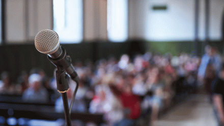 A microphone on a stage in front of a congregation.