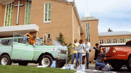 A diverse group of people washing cars in front of a church.