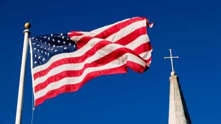 The American flag flying in front of a church steeple.