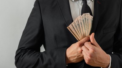 Man in black suit putting cash in his coat pocket.