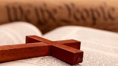 A wooden cross lying upon an open Bible in front of the Preamble to the US Constitution.