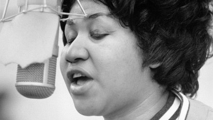 A black-and-white photo of Aretha Franklin singing into a recording studio microphone.
